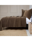 Diamond-quilted brown cotton velvet coverlet by POM POM with matching pillow on a woven rug.
