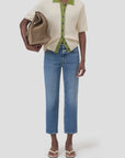 A person wearing CLOSED's Milo cream short-sleeve shirt with green trim, blue straight-leg jeans, white sandals, and carrying a large brown tote bag under their arm stands against a plain white background.