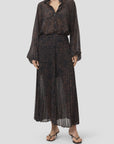 Closed pleated skirt and sheer dark patterned blouse, styled with black sandals; minimal backdrop, Bungalow Furniture.