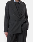 A person models the CLOSED Fitted Doublebreasted Blazer in dark gray with matching trousers, styled over a black top and light blue collared shirt, standing against a plain white background with one hand in their pocket.