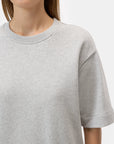 A woman wears the CLOSED Felpa Dress, a light gray, short-sleeve crew neck sweatshirt made of 100% cotton. She's shown from shoulders to mid-torso against a white background, with partially visible face and straight brown hair.