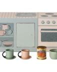 The Maileg Kitchen counter by Maileg features a retro-style cardboard stove and oven backdrop, pastel cups and plates, a white pitcher, green saucepan, and a "Pomodori" can—perfect for SuitCasa mouse-approved meals.