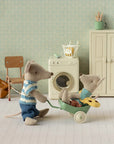 Little Brother Mouse with bag by Maileg pushes a wheelbarrow in a miniature laundry room, playful and charming scene.