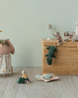 A wicker toy chest with plush animals, a toy lamp, and a miniature tea set stands near the Maileg Trolley by Maileg. Soft linen cushions and stuffed animals are scattered on the floor, creating a cozy and washable play space.
