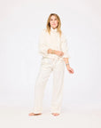 A person with long, light brown hair stands barefoot on a white background, wearing the Kerri Rosenthal Denim Jacket in Cloud styled with wide-leg white denim pants and rolled sleeves.