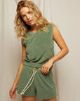 A woman with wavy blonde hair wears Perfectwhitetee's Summer Loop Terry Sweat Shorts and a matching green sleeveless top, standing in front of a plain light-colored fabric backdrop.