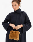 Brown shearling Clare Vivier Emma bag with drawstring closure held by a person in a navy wool coat.