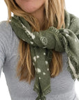 Olive green KR Cashmere Bandana with white heart pattern and frayed edges worn around the neck.