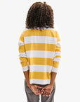 A person with curly hair, viewed from behind, wears a 100% cotton Clare Vivier yellow and white striped long sleeve tee and gray pants, holding their hands behind their back.
