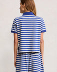 A person faces away, wearing Denimist's SHRUNKEN POLO—a blue and white striped cotton polo t-shirt and matching shrunken-fit shorts—against a plain light background.