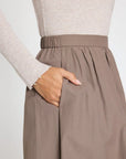 A person wearing a beige ribbed long-sleeve top and the BROCHU WALKER LOTI BUBBLE SKIRT—a modern, high-waisted taupe midi with an elastic waistband—has their right hand in the skirt pocket.