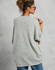 A woman with curly hair in a messy bun models the Mamene Boyfriend Tee, paired with blue jeans and glasses, standing with her back to the camera and turning her head to the side against a light gray background.