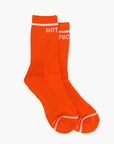 The Baby Steps crew socks by Mother feature a bright orange ribbed design with white accents at the top and toes, plus bold "MOT" and "FUC" in white, making them versatile essentials for year-round wear.