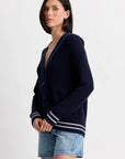 A person wears the One Grey Day Chelsea Cardigan, a women's navy knit cardigan with white and blue trim, paired with light blue denim shorts, standing against a plain white background.