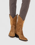 A person wearing ONCEPT’s Winslow Boot—western-inspired, premium-crafted with pointed toes and dark heels—paired with fitted gray pants, stands before a light background.
