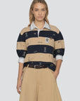 A woman wears the Sea New York Juliet SS Rugby with puff sleeves over a white collared shirt, paired with beige wide-leg pants and a dark braided belt, standing facing forward with one hand in her pocket.