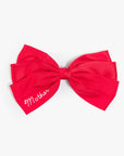 Red silk hair bow by THE BOW with white embroidered script detail on one tail.