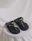Black adjustable Flowze FLO sandals with green rope straps displayed on a white-draped round surface.