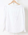 White cotton long-sleeve top by Rachel Comey on wooden hanger against a white wall.