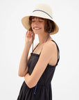 Clare Vivier Romy Hat with sail cord strap on woman in black dress, simple neutral background, stylish look.