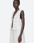 A woman with short hair wears the Lois Twill Vest by Sea New York, an oversized cotton vest with front pockets and ties, paired with a matching white skirt against a plain light background.