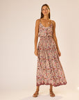 A woman wears the natalie martin Bella Skirt, a colorful floral rayon piece with an elastic waist, styled with flat sandals and layered necklaces. She has long hair and stands against a softly lit plain background.