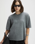 The Cashmere Oversized Tee in soft grey by Sold Out NYC, styled with black bag and sunglasses against light background.