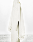 A pair of cream-colored, oversized Lucky Rabbits sweatpants hanging from a hook in a bungalow in Scottsdale, Arizona against a white wall with a gray concrete floor, displaying the text "lucky rabbits" near the bottom. Brand: Free City (sparrow, LLC)