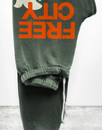 The FREECITY Large Sweatpant by Free City features a lightweight French terry design with an orange "FREE CITY" print and white dove illustration on a plain gray background.