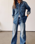 Indoors, someone wears The Western Shirt by Hey Gang with wide-leg blue jeans, creating a casual, relaxed look in Japanese denim with a subtle vintage finish. Sleeves are rolled and the person's face isn't visible.