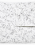 The John Robshaw Hand Stitched Coverlet Queen is made of white organic cotton with small black dashes and plus signs, shown folded to feature its reversible design.