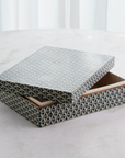 The Global Views Interwoven Box LG, featuring a geometric blue and white design, rests on a light surface with its lid partially open to show the empty interior.