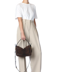 A person in a white t-shirt and high-waisted beige trousers holds the Jerome Dreyfuss Pepito Bag, a brown leopard print handbag with black handles and gold accents. The person's head is not visible.