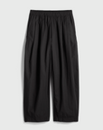 The Apiece Apart Spa Pleat Pant, crafted from black organic cotton, features a wide-leg cut, elastic waistband, and side pockets, shown flat on a light gray background.