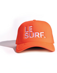 The Ping Pong Surf Club Le Surf Hat is an orange mesh trucker cap with white mesh sides and "LE SURF." in crisp white embroidery on the front, shown on a white background.