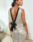 Sleeveless gold sequin mini dress with low V-back and black velvet waist bow by Hunter Bell NYC.