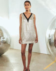 Wilkinson sleeveless gold sequin mini dress with black V-neck trim and pumps for evening wear.