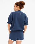 Blue Clare Vivier oversized short sleeve sweatshirt shown from the back, modeled by woman with curly hair in a bun.