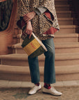 The Striped Pouch in green and yellow cotton canvas held by a person in a leopard print poncho and jeans.