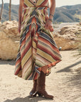 A person outdoors wears The Rhythm Skirt by The Great Inc., styled with brown cowboy boots, standing on rocky terrain with mountains in the background.
