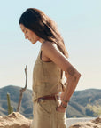 A woman with long brown hair and an upper arm tattoo stands outdoors in profile, wearing The Great Inc.'s The Suit Vest. Desert mountains and cacti are in the scenic background.