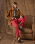 The Fleece Stadium Sweatpants in bright red worn with a brown suede jacket while seated in a leather armchair.