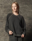 The Great Inc. Rehearsal Sweatshirt and pants in gray, relaxed fit, modeled against a textured gray backdrop.