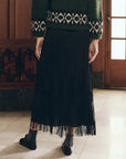 Black midi fringe skirt by The Great Inc. paired with a green sweater and dark shoes in a 1920s-inspired style.