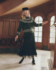 The Great Inc. black tiered fringe midi skirt and green fair isle sweater worn in a wood-paneled hallway.