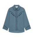 The Great Inc.’s The Pajama Shirt is a blue long-sleeve button-up with a rounded collar, black piping on the chest, collar, and cuffs, and features a relaxed fit with classic sleepwear styling.