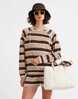 A woman wearing The Terry Franny sweatshirt by Kule, paired with matching shorts, a black bucket hat, sunglasses, and holding a large cream canvas tote against a plain background.