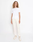 A person with curly blonde hair, a plain white T-shirt, cream shoes, and Kule’s The Terry Sweatpants stands against a white background.