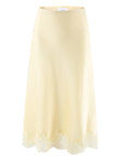 The Slip Skirt by THE SHIRT is a light yellow poly satin skirt with a subtle sheen and delicate lace hem, shown on a plain white background.