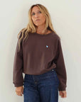 Kerri Rosenthal True Sweatshirt in chocolate brown with blue heart paired with dark blue jeans.